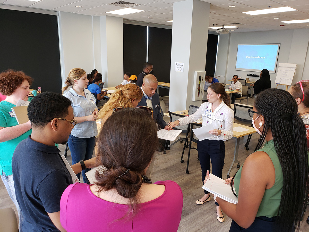 A group of people standing in a meeting room handing around some documents